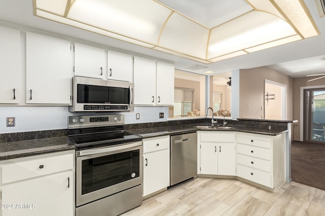 kitchen featuring appliances with stainless steel finishes, white cabinetry, dark stone counters, and sink