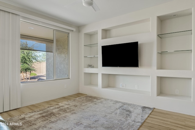 unfurnished living room with built in shelves, light hardwood / wood-style floors, and ceiling fan