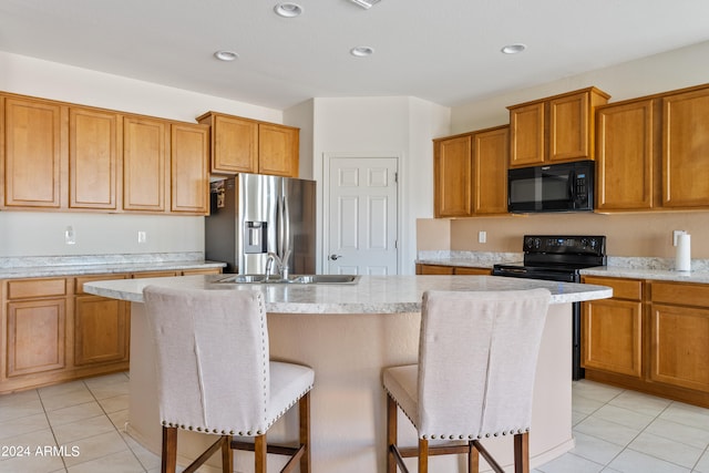 kitchen featuring black appliances, light tile patterned flooring, a center island with sink, and a kitchen breakfast bar