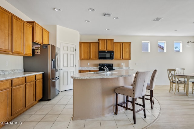 kitchen with sink, a kitchen bar, light tile patterned floors, a center island with sink, and stainless steel refrigerator with ice dispenser