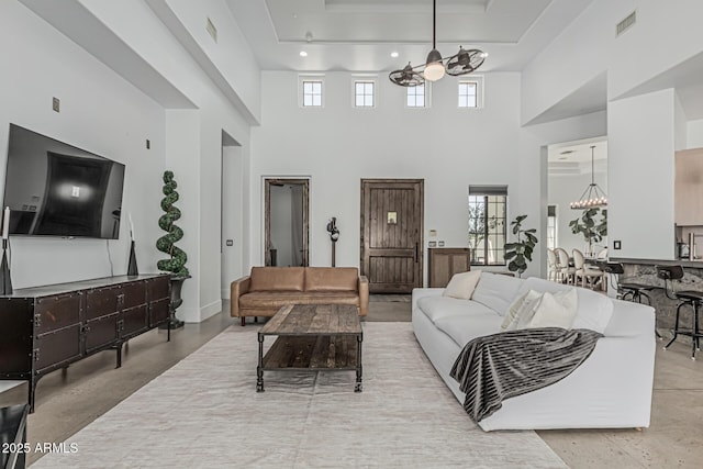 living room with visible vents, a raised ceiling, a towering ceiling, and a notable chandelier