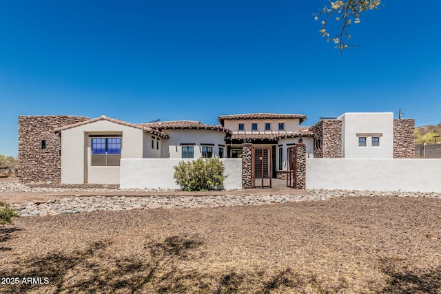 view of front facade featuring a tiled roof, a fenced front yard, stucco siding, and stone siding