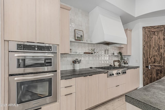 kitchen with light brown cabinetry, dark countertops, appliances with stainless steel finishes, and custom exhaust hood
