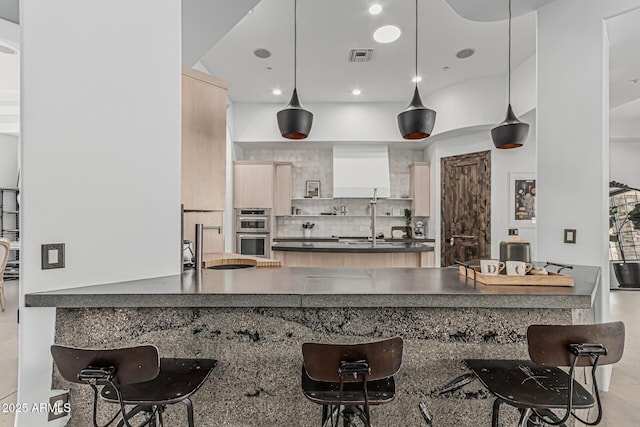 kitchen featuring decorative backsplash, a kitchen breakfast bar, visible vents, dark countertops, and a peninsula
