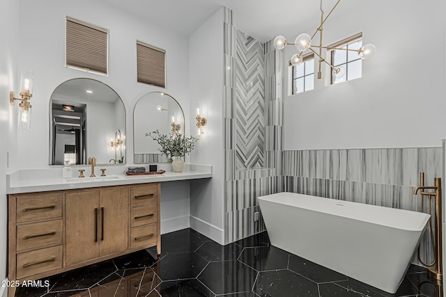 full bathroom with a notable chandelier, a freestanding bath, vanity, baseboards, and tile walls