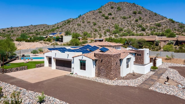 view of front of property featuring a garage, stucco siding, roof mounted solar panels, a mountain view, and driveway