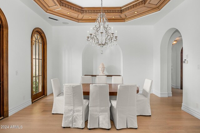 dining area featuring a tray ceiling, light hardwood / wood-style floors, a chandelier, and crown molding