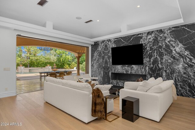 living room with an inviting chandelier, light hardwood / wood-style floors, and a high end fireplace