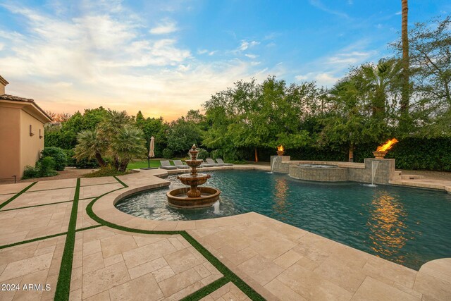 pool at dusk featuring a patio, an in ground hot tub, and pool water feature