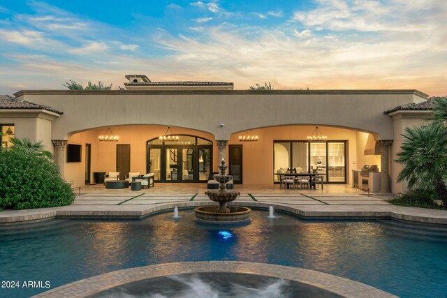 back house at dusk featuring pool water feature, outdoor lounge area, a patio area, and french doors