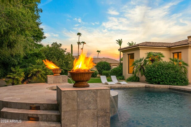 pool at dusk with a patio and a fire pit