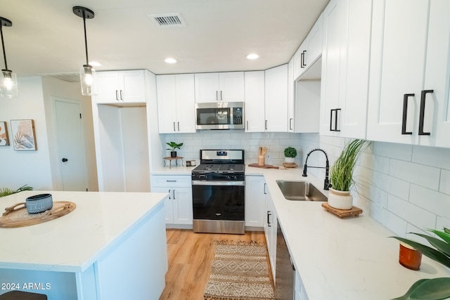 kitchen with hanging light fixtures, stainless steel appliances, sink, white cabinets, and light hardwood / wood-style floors