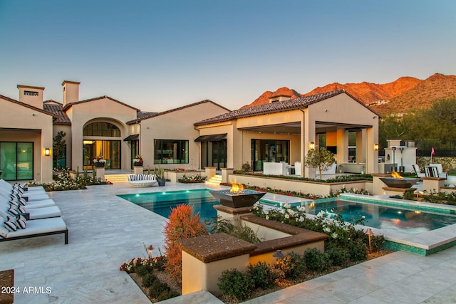 pool at dusk with a patio, a hot tub, and a mountain view