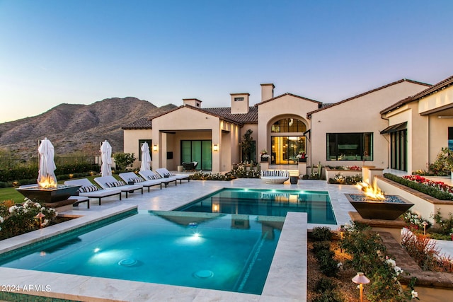 view of swimming pool featuring a patio area, a fire pit, a mountain view, and an in ground hot tub