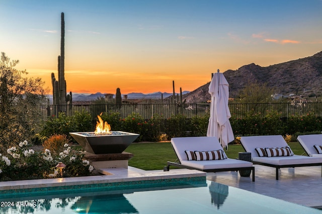 pool at dusk with a mountain view, an outdoor fire pit, a yard, and a patio area