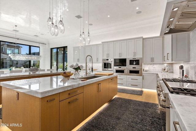 kitchen featuring light wood-type flooring, wall chimney range hood, an island with sink, and white cabinetry