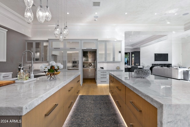 kitchen with a kitchen island, light stone counters, light hardwood / wood-style floors, and hanging light fixtures