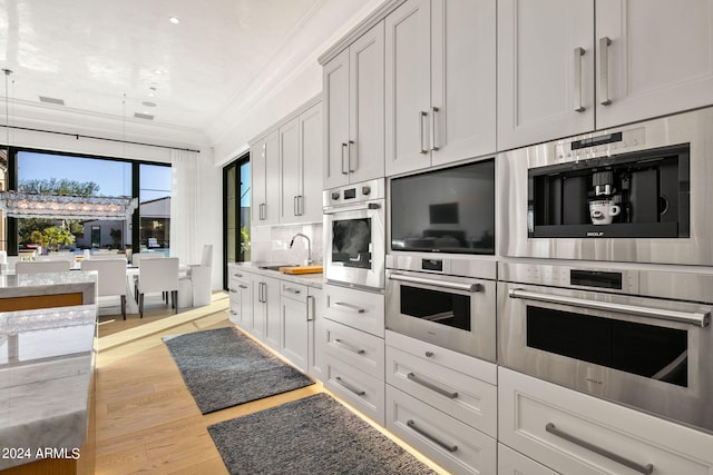 kitchen featuring light wood-type flooring, double oven, white cabinetry, ornamental molding, and sink