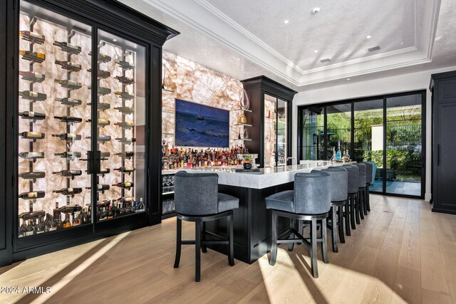 wine cellar with ornamental molding, light hardwood / wood-style floors, and a raised ceiling