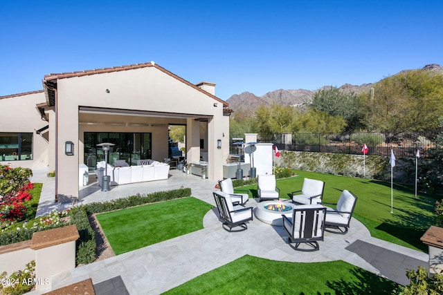 rear view of property with a patio area, an outdoor living space with a fire pit, a mountain view, and a lawn