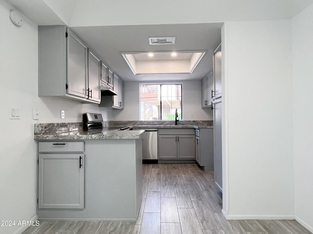 kitchen featuring gray cabinetry, sink, stainless steel appliances, a raised ceiling, and light hardwood / wood-style floors