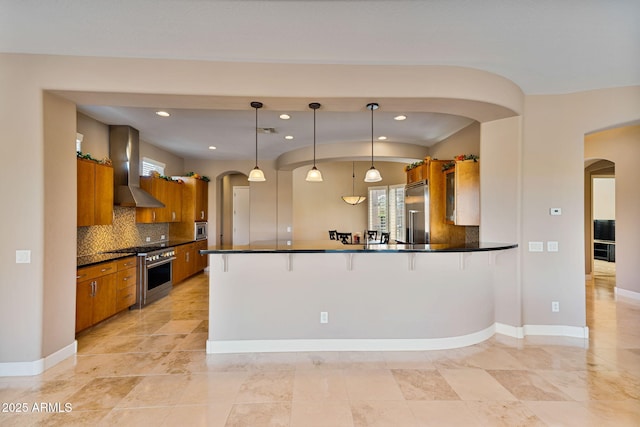 kitchen featuring wall chimney exhaust hood, tasteful backsplash, kitchen peninsula, decorative light fixtures, and high end appliances