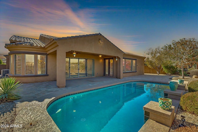 pool at dusk featuring ceiling fan and a patio area