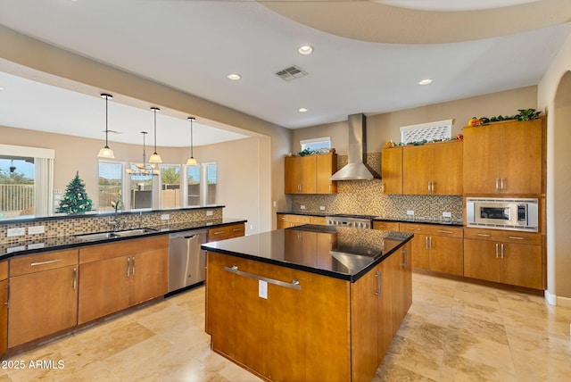 kitchen featuring sink, hanging light fixtures, wall chimney range hood, a kitchen island, and appliances with stainless steel finishes