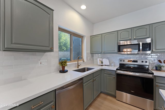 kitchen with backsplash, sink, appliances with stainless steel finishes, and light hardwood / wood-style flooring