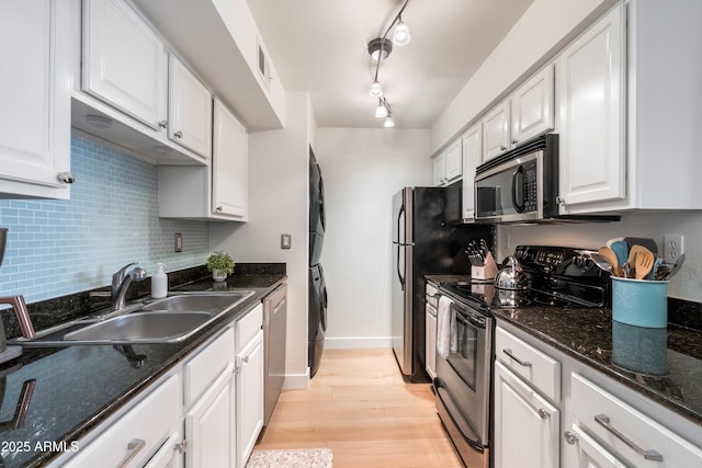 kitchen featuring white cabinets, sink, rail lighting, stacked washing maching and dryer, and stainless steel appliances