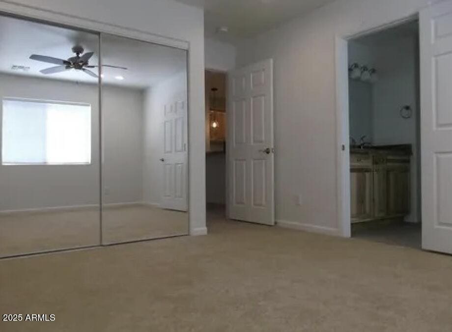 unfurnished bedroom with a closet, carpet flooring, baseboards, and ensuite bathroom