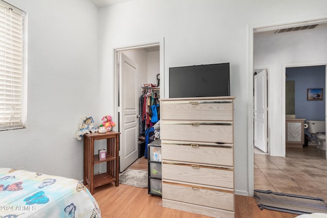 bedroom with ensuite bathroom, a closet, and light wood-type flooring