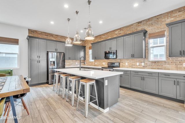 kitchen featuring pendant lighting, sink, a kitchen island with sink, gray cabinetry, and stainless steel appliances