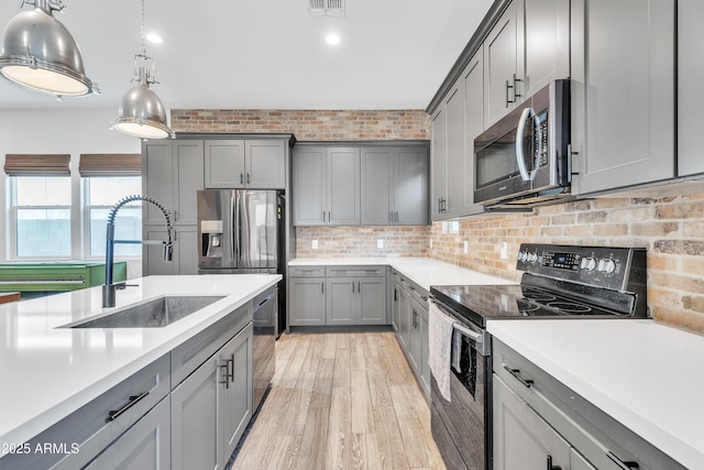 kitchen featuring sink, gray cabinetry, light wood-type flooring, pendant lighting, and stainless steel appliances