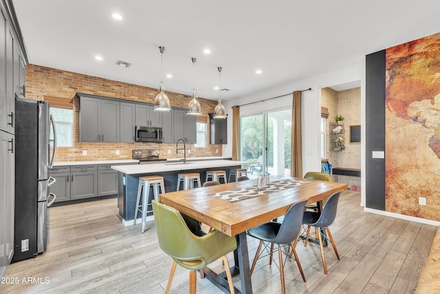 dining space with brick wall, light hardwood / wood-style floors, and sink