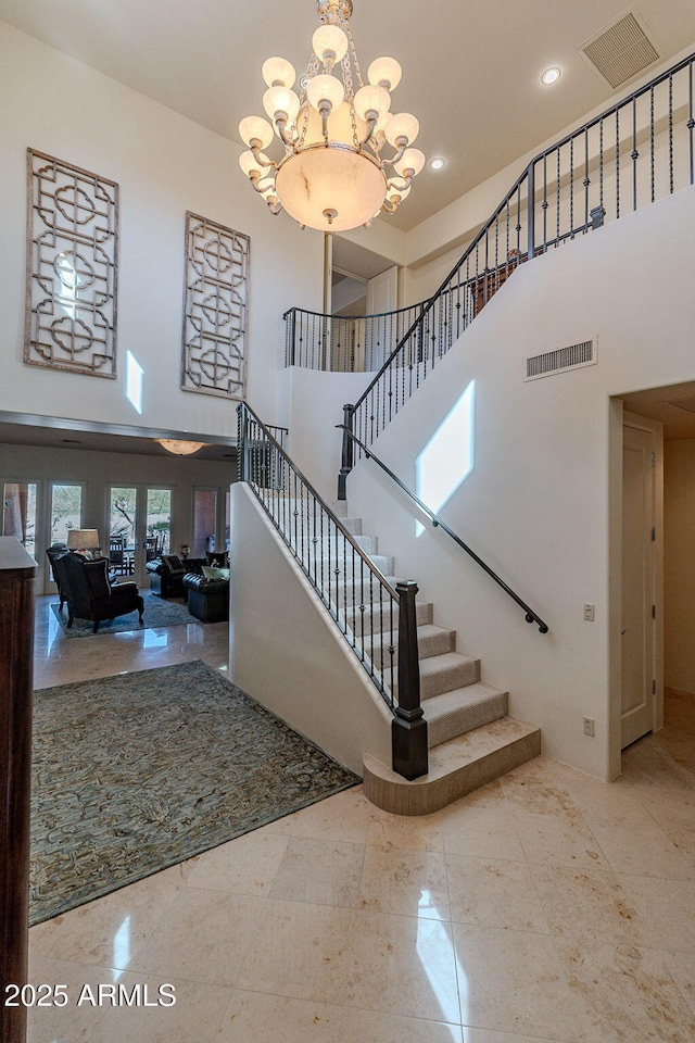 stairway with a towering ceiling, an inviting chandelier, and visible vents