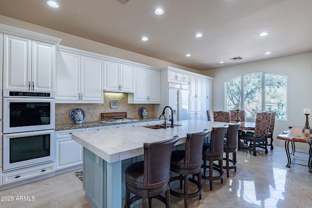 kitchen featuring white appliances, a sink, visible vents, decorative backsplash, and a kitchen bar