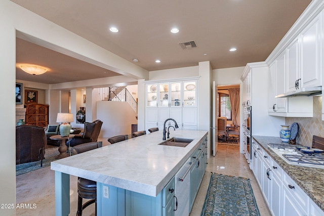 kitchen featuring white cabinets, a breakfast bar area, a sink, a kitchen island with sink, and backsplash