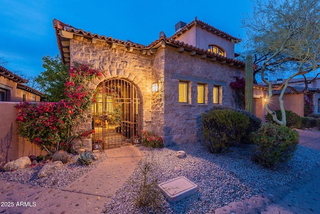 mediterranean / spanish house featuring stone siding, a gate, and fence