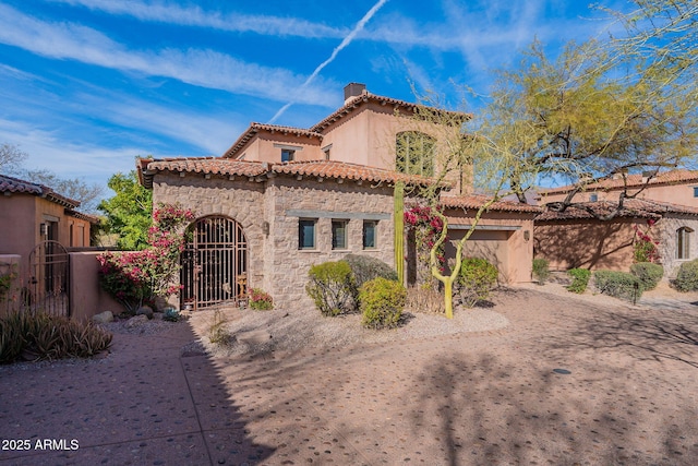 mediterranean / spanish house with stone siding, a tile roof, a chimney, a gate, and fence