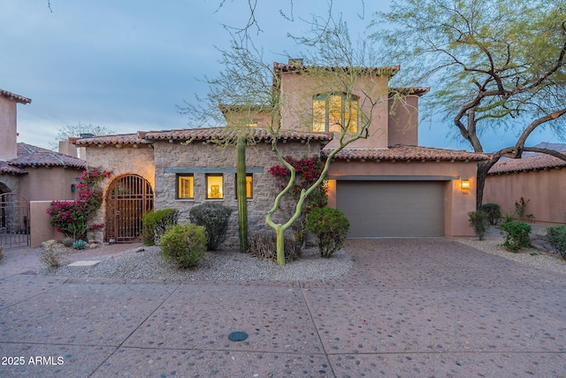 mediterranean / spanish-style home with driveway, a garage, stone siding, a gate, and stucco siding