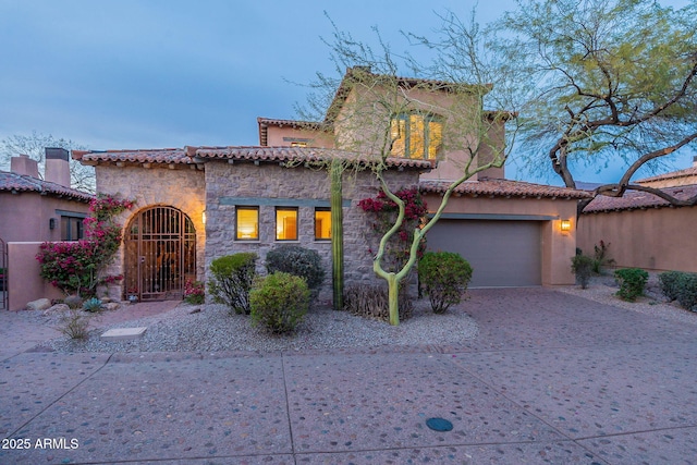 mediterranean / spanish house featuring stone siding, decorative driveway, a tiled roof, and a garage