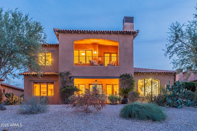 mediterranean / spanish house with a balcony, a chimney, and stucco siding