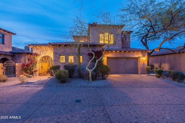 mediterranean / spanish-style house featuring a garage, a gate, concrete driveway, and stucco siding