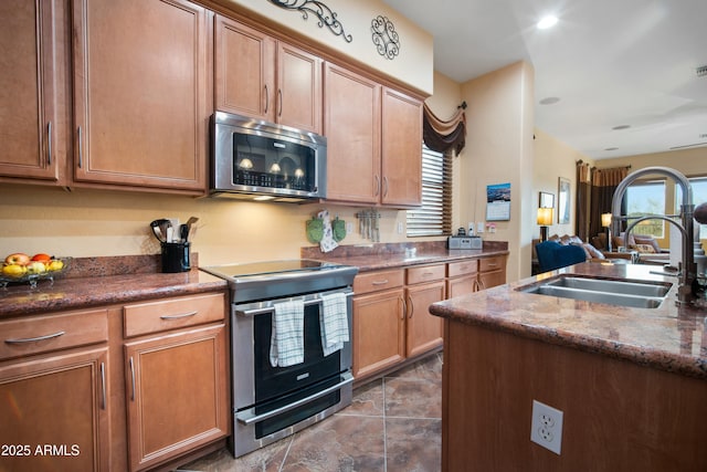 kitchen featuring appliances with stainless steel finishes, brown cabinets, a sink, and dark stone countertops