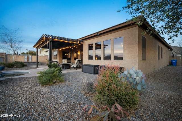 rear view of property featuring stucco siding, a patio area, fence, a pergola, and a fire pit