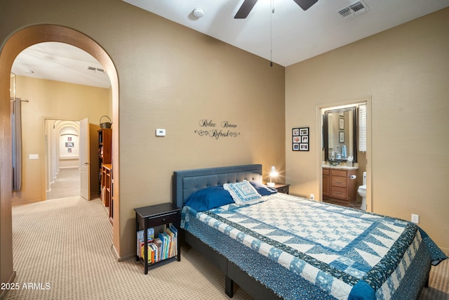 bedroom featuring arched walkways, ensuite bathroom, visible vents, and light colored carpet