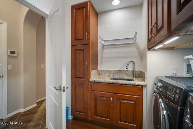 clothes washing area featuring arched walkways, washing machine and clothes dryer, cabinet space, a sink, and baseboards