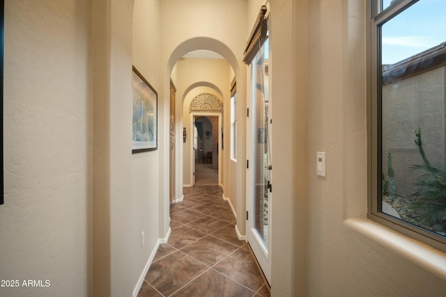 hall with arched walkways, dark tile patterned flooring, and baseboards