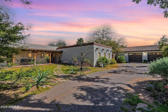 view of front facade featuring a garage, stucco siding, and gravel driveway